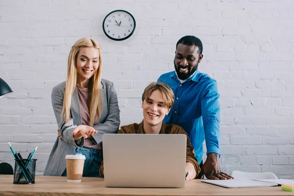 Smiling multiethnic group of business colleagues watching at laptop screen in modern office — Stock Photo