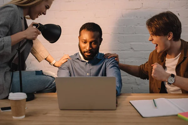 Compañeros de trabajo amenazante y brillo de la lámpara en la cara de los empresarios afroamericanos utilizando el ordenador portátil - foto de stock
