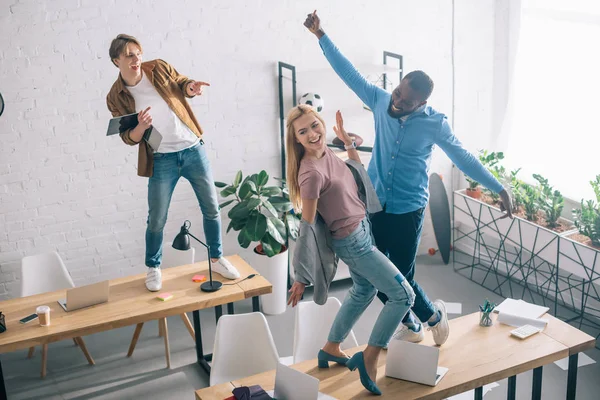 Vista de ángulo alto de compañeros de negocios multiétnicos felices bailando y divirtiéndose en la oficina moderna - foto de stock