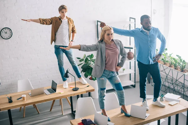 Blick aus der Vogelperspektive auf fröhliche multiethnische Geschäftskollegen, die Spaß haben und auf Tischen im modernen Büro tanzen — Stockfoto