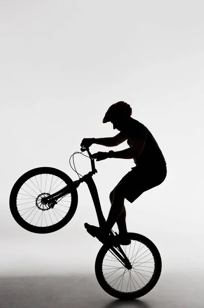 Silhouette eines Trial-Bikers steht auf Hinterrad auf weiß — Stockfoto