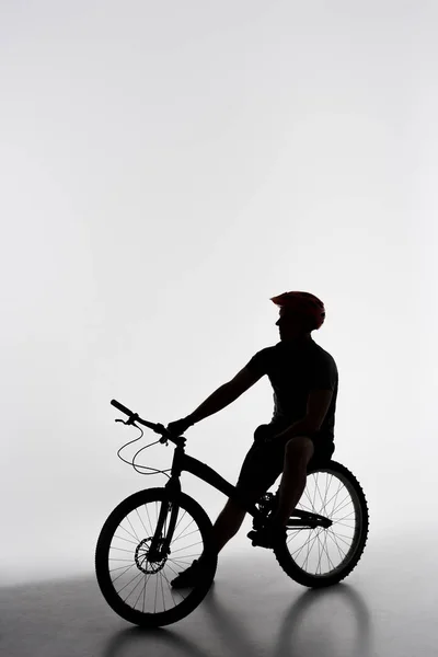 Silhouette of trial biker relaxing on bicycle on white — Stock Photo