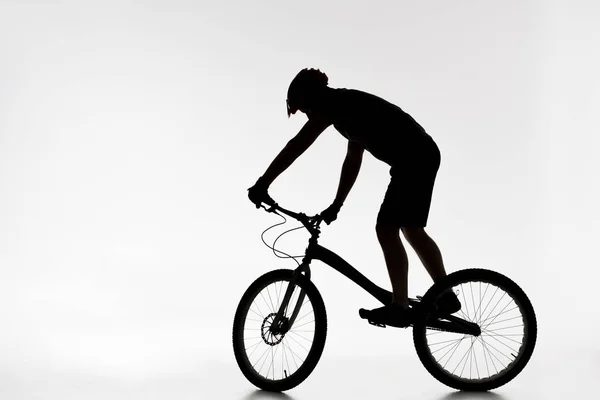 Silueta del motociclista de trial en el casco de equilibrio en bicicleta en blanco - foto de stock