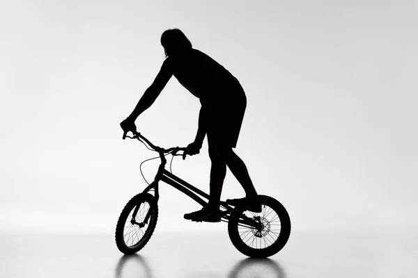 Silhouette of trial biker balancing on bicycle on white — Stock Photo