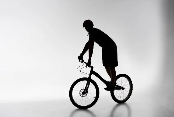 Силует пробного велосипедиста в шоломі балансування на велосипеді на білому — стокове фото
