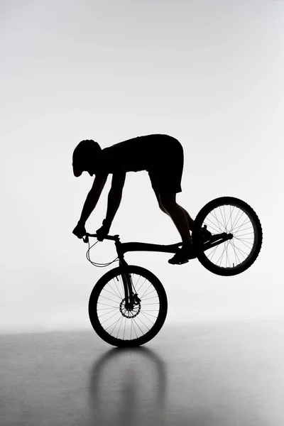 Silhouette of trial biker performing front wheel stand on white — Stock Photo