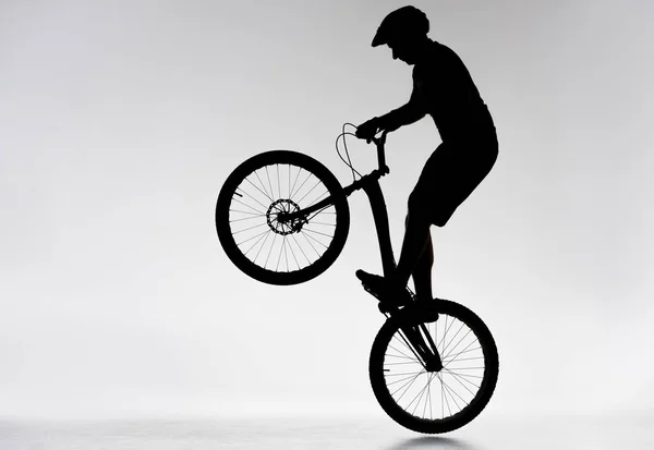 Silhouette of trial biker performing bunny hop on white — Stock Photo