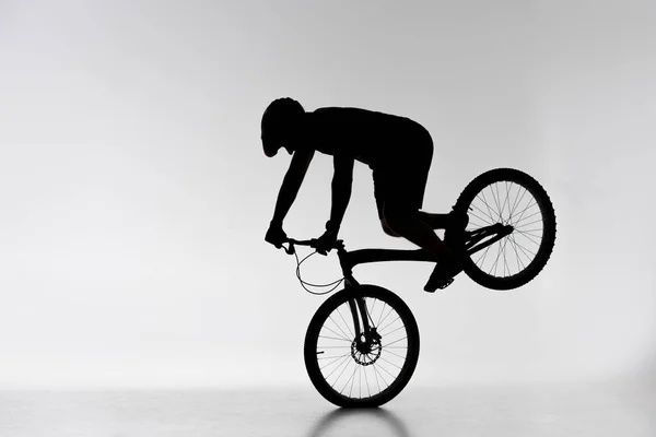 Silhouette of trial cyclist performing front wheel stand on white — Stock Photo