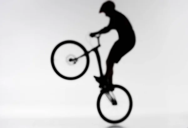 Colpo sfocato di silhouette del biker di prova che esegue bunny hop su bianco — Foto stock