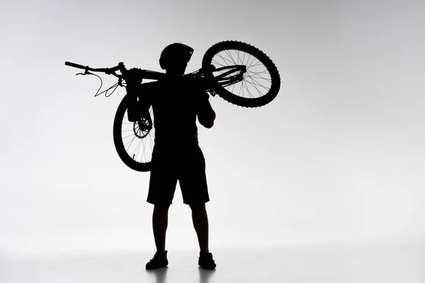 Silhouette of trial biker holding bicycle on shoulders on white — Stock Photo