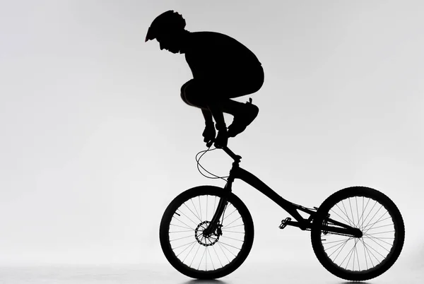 Silhouette of trial biker standing on handlebars with hands on white — Stock Photo