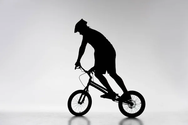 Silhouette of trial cyclist balancing on bicycle on white — Stock Photo