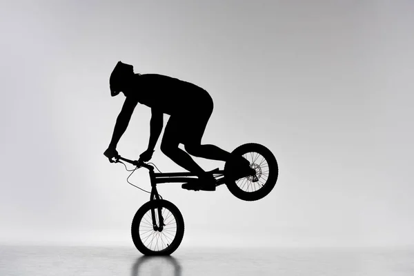Silhueta do ciclista experimental que executa o suporte da roda dianteira no branco — Fotografia de Stock