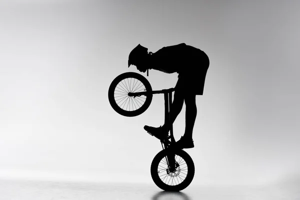 Silueta del motociclista de trial realizando acrobacias de equilibrio en bicicleta en blanco - foto de stock