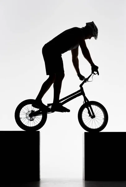 Silhouette of trial cyclist balancing on two stands on white — Stock Photo