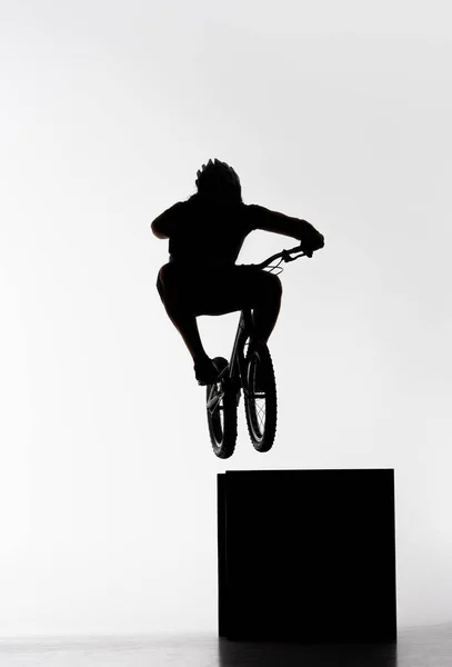 Silhouette del biker di prova che salta sul cubo su bianco — Foto stock