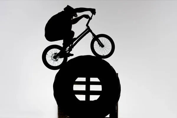 Silhouette of trial cyclist balancing on tractor wheel on white — Stock Photo