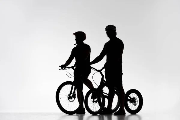 Siluetas de los ciclistas de trial en cascos con bicicletas en blanco - foto de stock