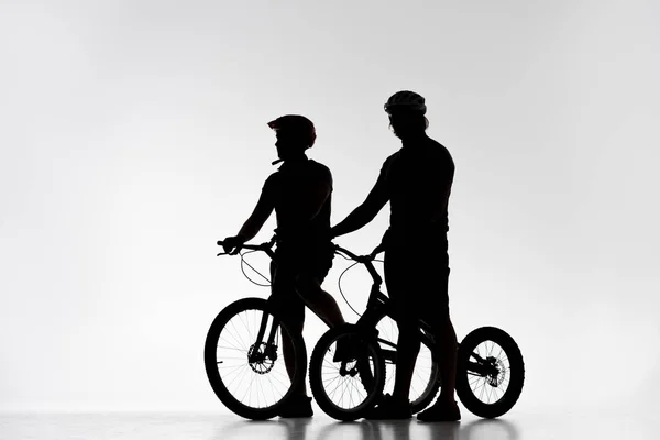 Silhouettes of trial bikers in helmets with bicycles on white — Stock Photo