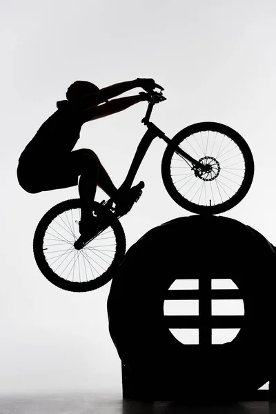 Silhouette of trial biker balancing on tractor wheel on white — Stock Photo