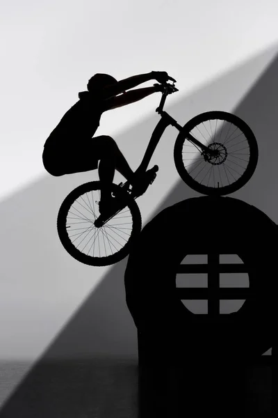 Silhouette of trial biker balancing on tractor wheel on grey — Stock Photo