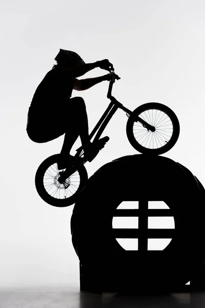 Silhouette of trial biker jumping on tractor wheel on white — Stock Photo