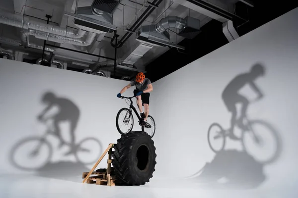 Young athletic trial biker balancing on tractor wheel — Stock Photo