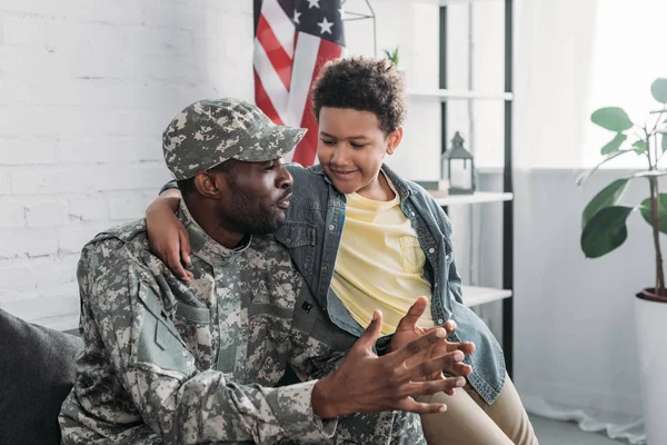 Afrikanischer amerikanischer Junge umarmt und hört seinem Vater in Armeeuniform zu — Stockfoto