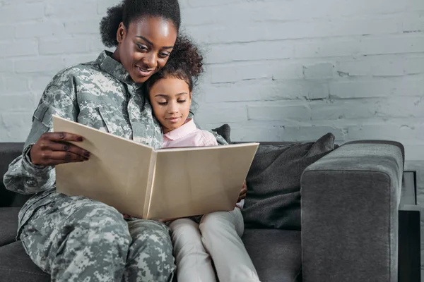 African american woman in camouflage clothes and child reading book — Stock Photo