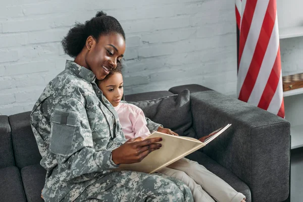 Mother soldier and african american child reading book — Stock Photo