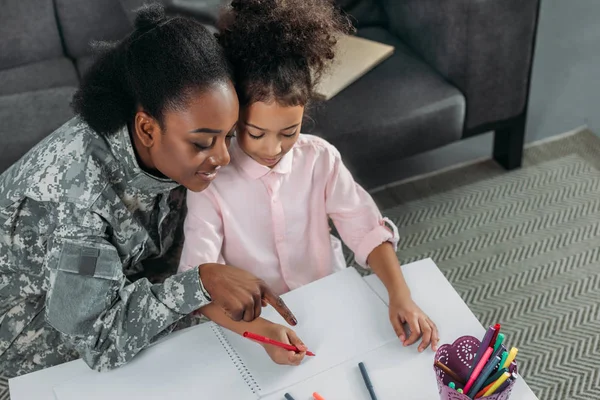 Afroamerikanerin in Tarnkleidung und Kind zeichnen zusammen — Stockfoto