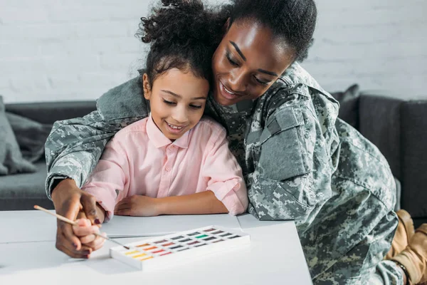African american female soldier with daughter drawing with watercolor paint — Stock Photo