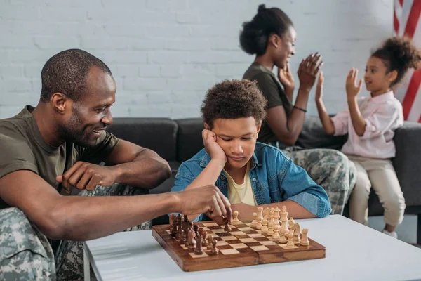 Young army soldier man playing chess with his son while mother and daughter playing together — Stock Photo