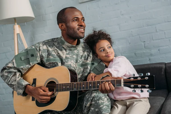 Padre in uniforme militare che suona la chitarra e abbraccia la figlia — Foto stock