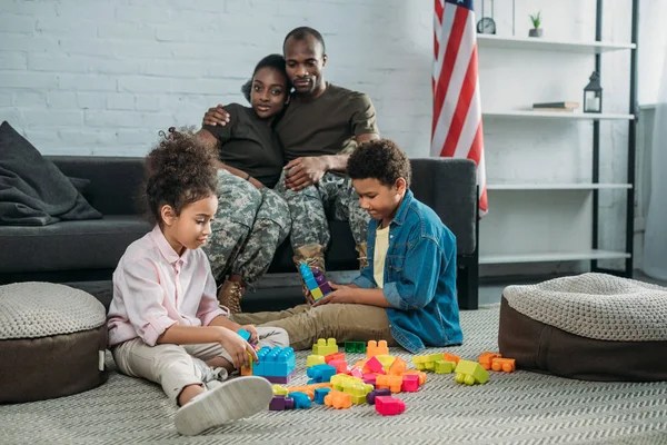 Parents in camouflage clothes looking at their children playing with cubes — Stock Photo