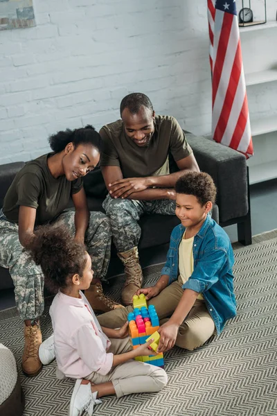 Mujer y hombre en uniforme militar mirando a sus hijos jugando con el constructor - foto de stock