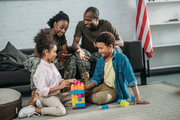 Africano americano homem e mulher soldados olhando para seus filhos brincando com cubos — Fotografia de Stock