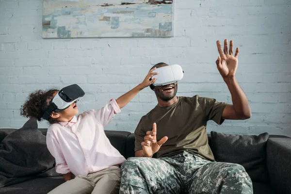 Soldado bonito em roupas de camuflagem com criança brincando com fones de ouvido de realidade virtual — Fotografia de Stock