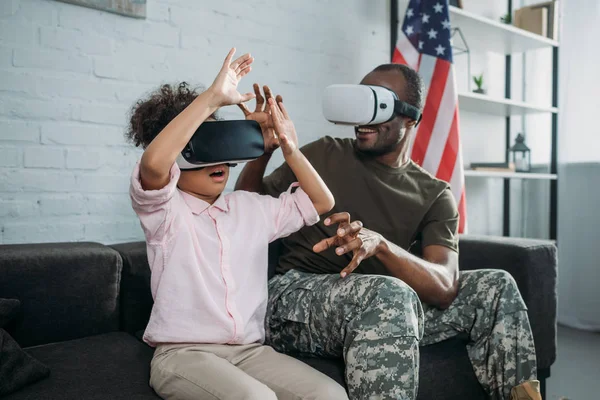Young male soldier in camouflage clothes and little daughter using vr glasses — Stock Photo