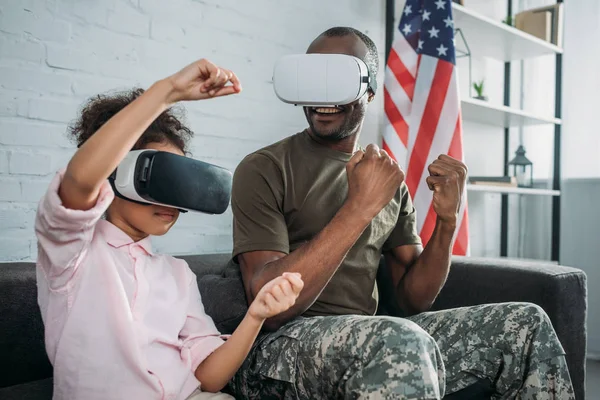 Família feliz com filha e pai em roupas do exército brincando com fones de ouvido de realidade virtual — Fotografia de Stock