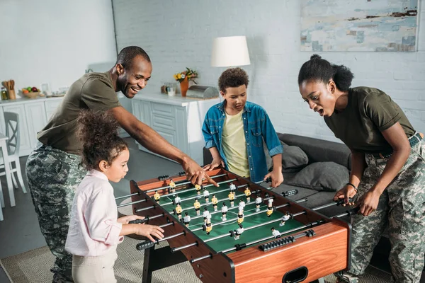 Woman and man in army uniform and cheerful kids playing table football — Stock Photo