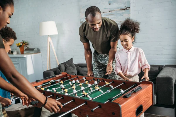 Los padres en ropa de camuflaje jugando futbolín con sus hijos - foto de stock