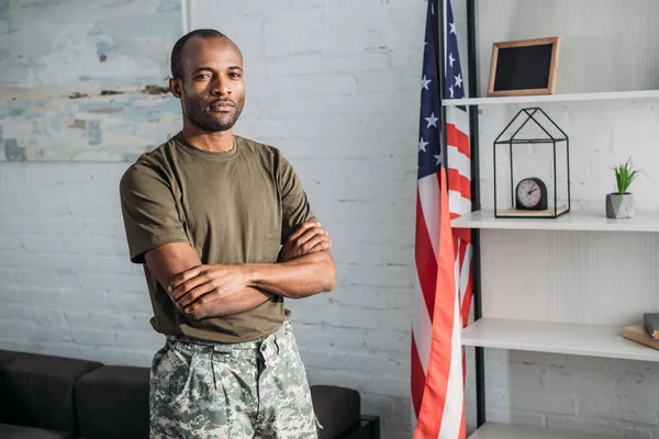 Hombre de confianza en ropa de camuflaje de pie en la habitación con bandera - foto de stock