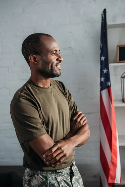 African american soldier with folded arms standing in room with flag — Stock Photo