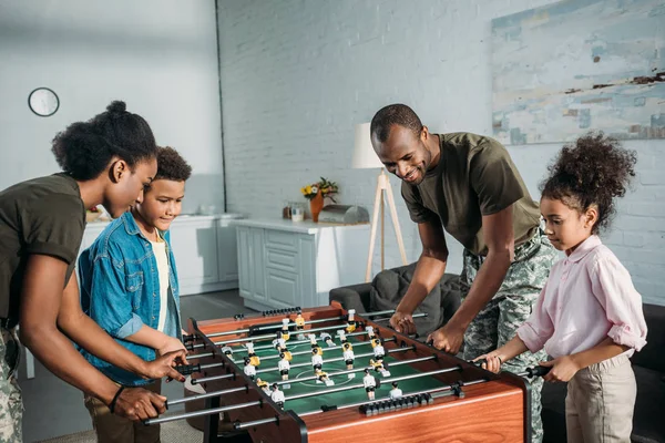 Happy family of soldier parents and african american kids playing table football — Stock Photo