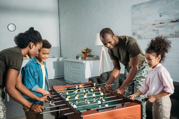 Familia feliz de padres soldados y niños afroamericanos jugando futbolín - foto de stock