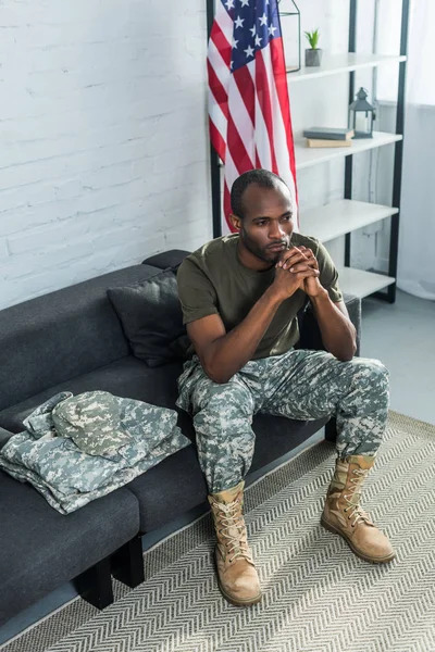 Продуманий солдат сидить на дивані з камуфляжним одягом — стокове фото