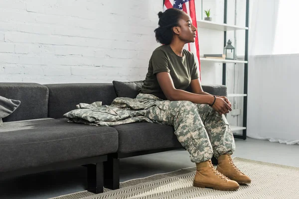 Young female soldier in camouflage clothes waiting on sofa in room — Stock Photo