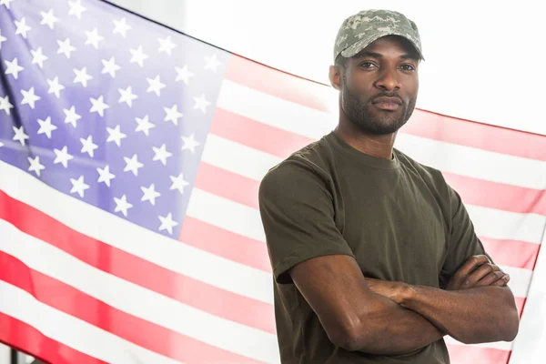 Guapo soldado afroamericano en ropa de camuflaje frente a nosotros bandera - foto de stock