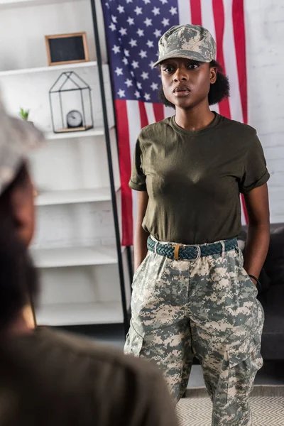 Atractiva mujer afroamericana en ropa de camuflaje posando junto al espejo - foto de stock